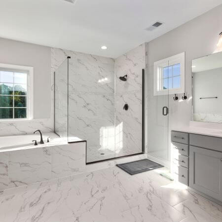 Bathroom Remodeling (4) A modern bathroom with a white bathtub, sink, and toilet. The walls are tiled in light gray with a large mirror above the sink.
